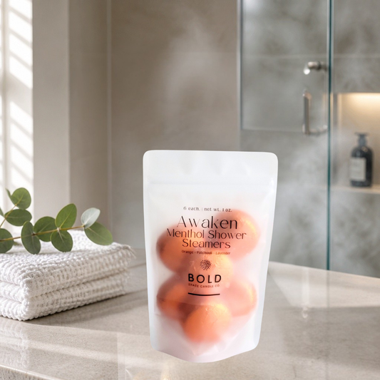 Pack of Awaken Menthol Shower Steamers on a bathroom counter with towels and a plant in the background.