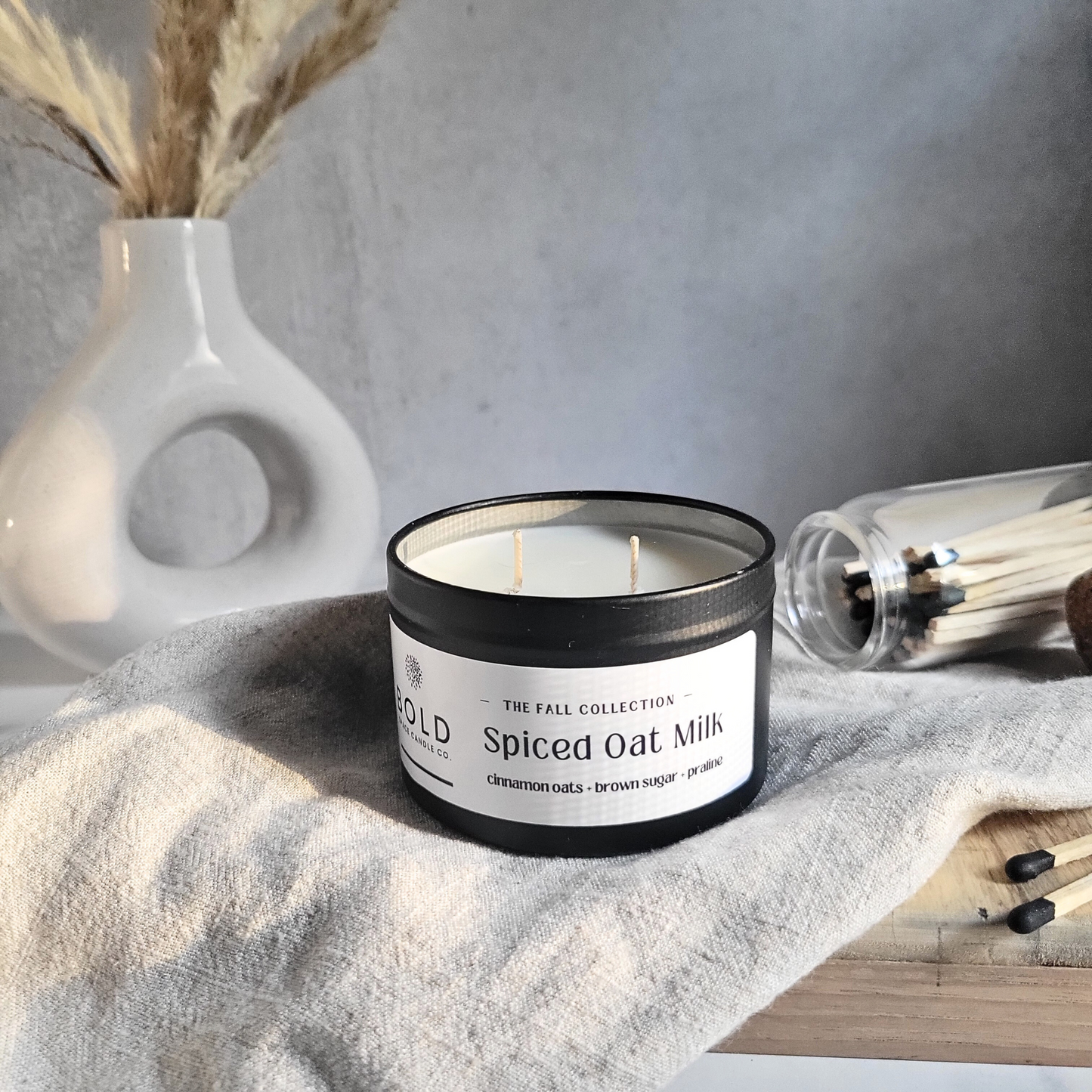 Candle labeled 'Spiced Oat Milk' from the 'The Fall Collection' on a textured surface with decorative elements.