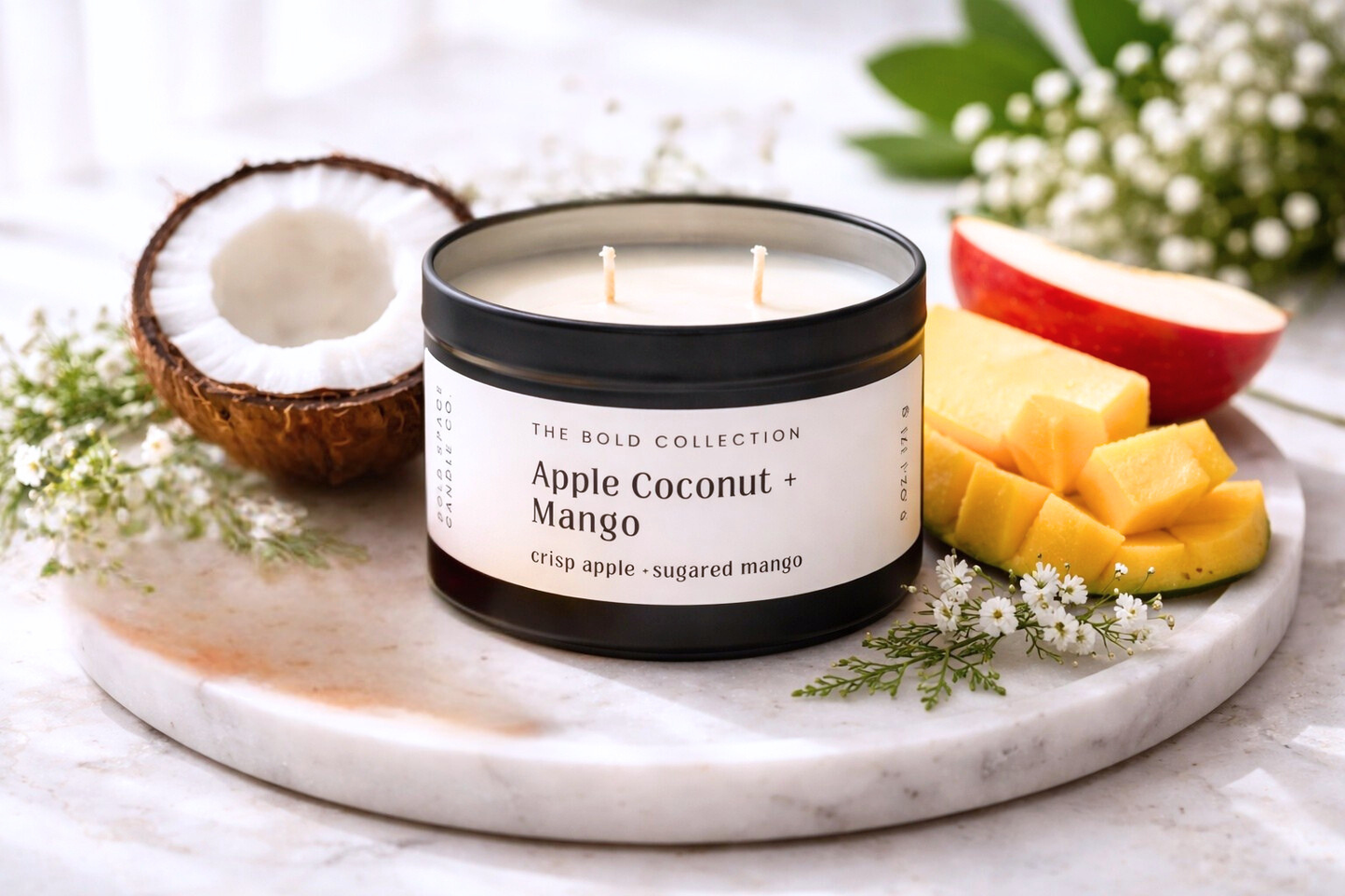 Candle labeled 'Apple Coconut Mango' on a marble tray with fruit and flowers