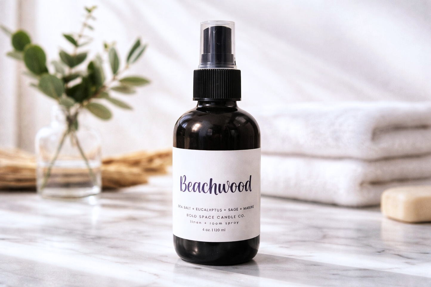 Black spray bottle labeled 'Beachwood' on a marble surface with a blurred background