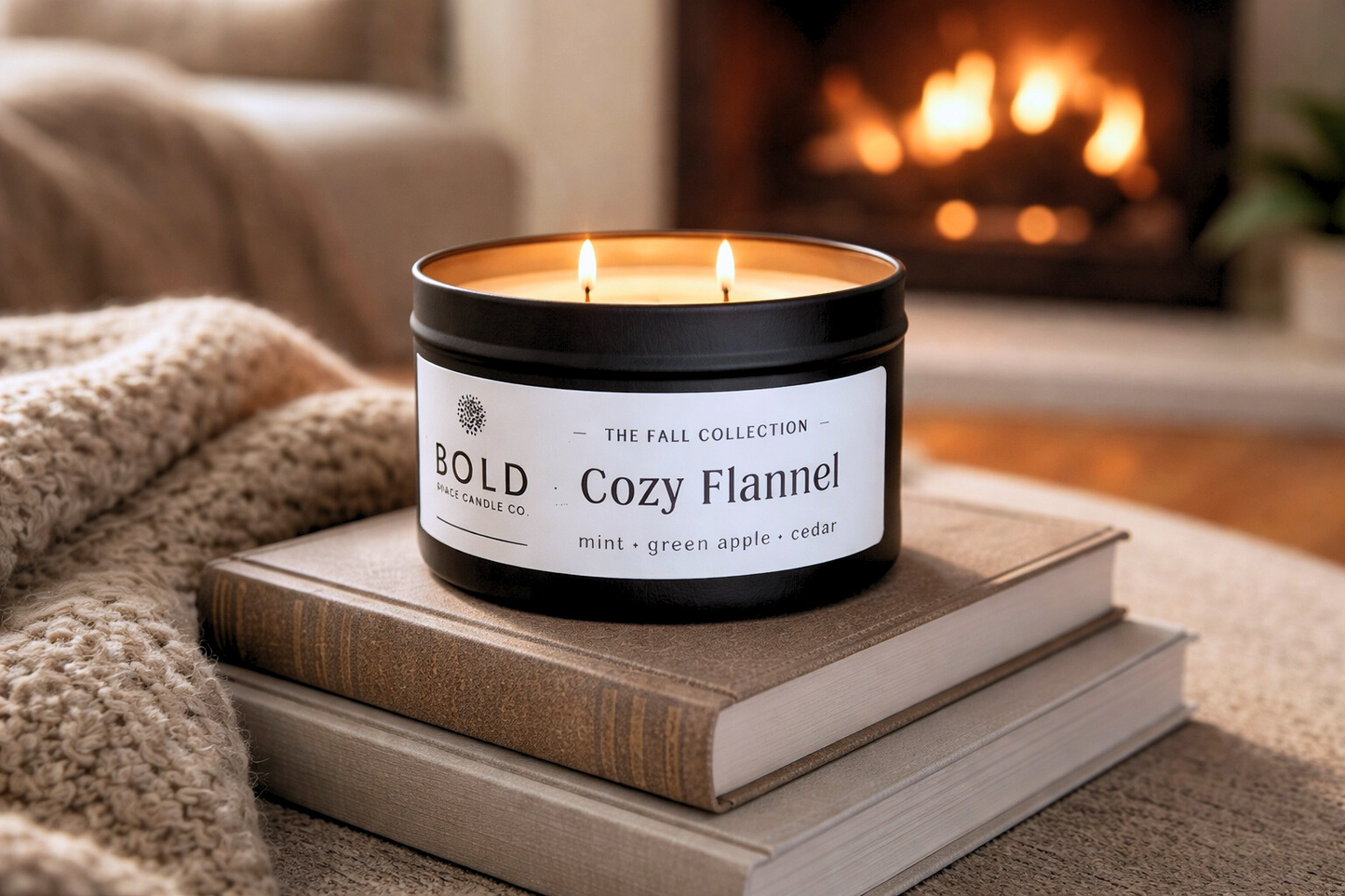 Candle labeled 'Cozy Flannel' on a stack of books with a fireplace in the background