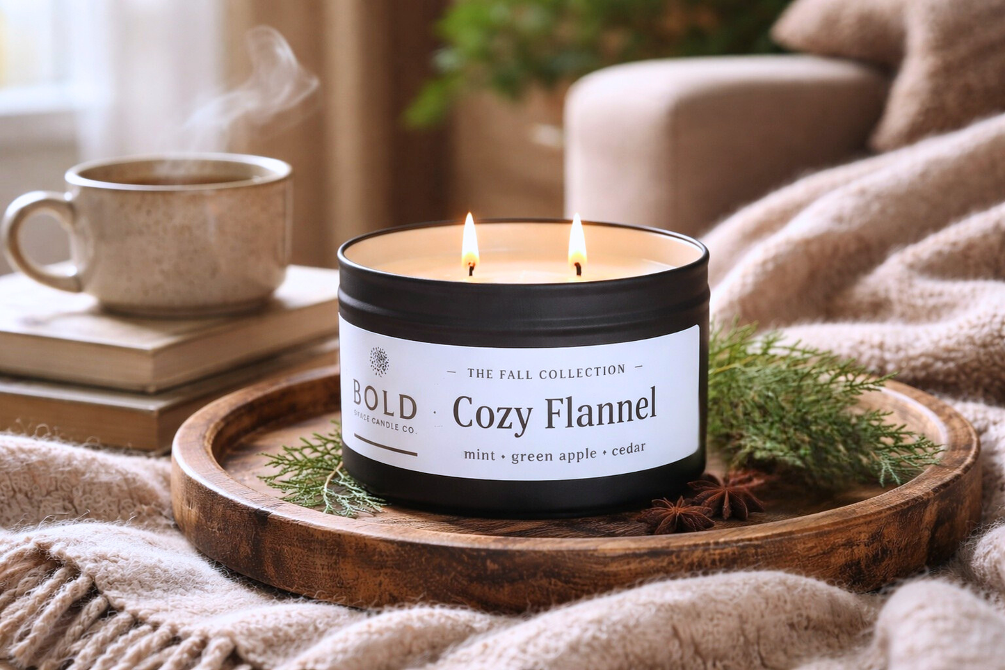 Candle labeled 'Cozy Flannel' on a wooden tray with a cup and books in the background