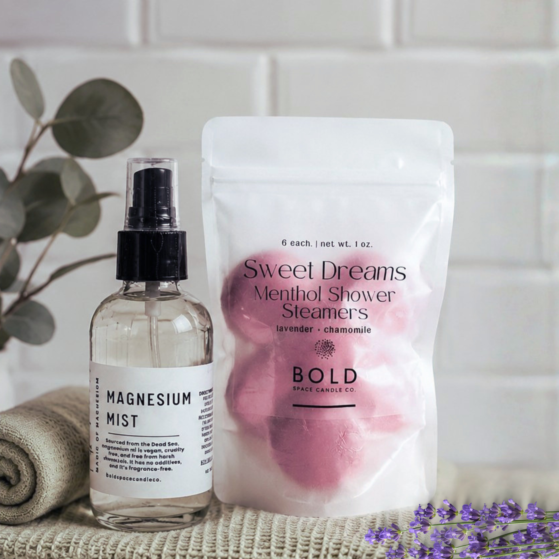 Bottle of magnesium mist and package of shower steamers on a surface with a plant and lavender in the background.