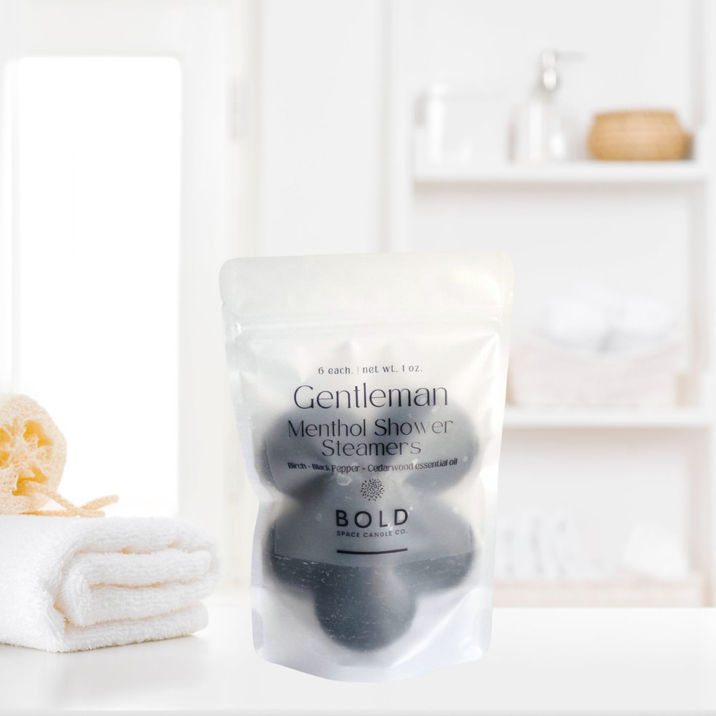 Gentleman birch black pepper cedarwood shower steamers pack on a bathroom countertop with towels.