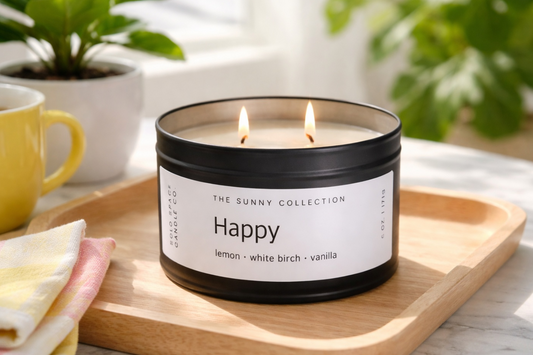 Sunny Collection 'Happy' candle on a wooden tray with a mug and plant in the background