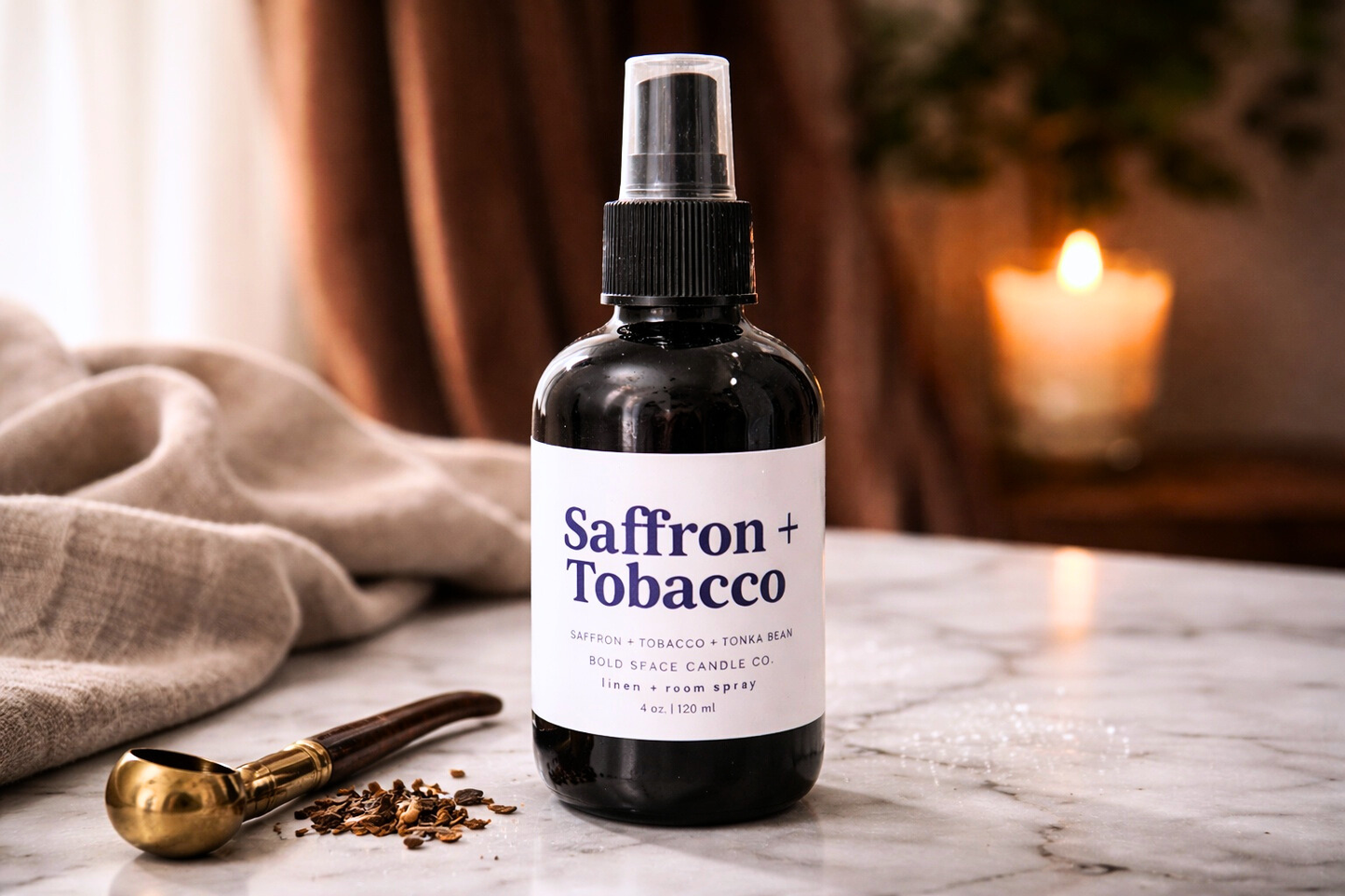 Saffron + Tobacco linen spray on a marble surface with a candle in the background.