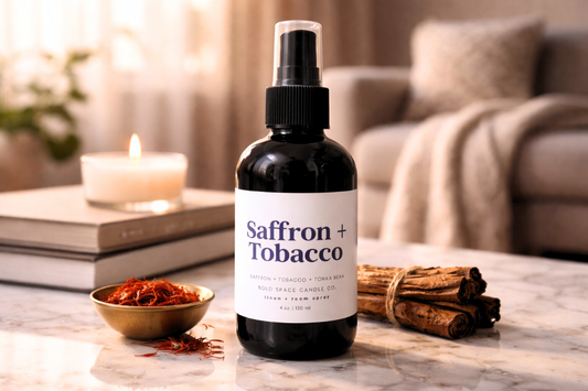 Saffron + Tobacco linen spray on a table with cinnamon sticks and saffron in a bowl.