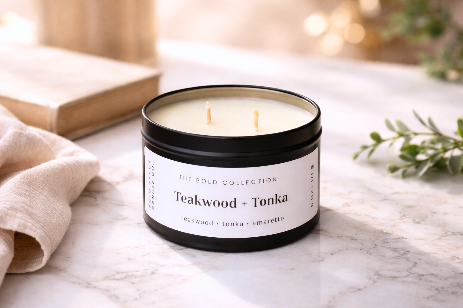 Candle in a black container labeled 'Teakwood + Tonka' on a marble surface with a blurred background.