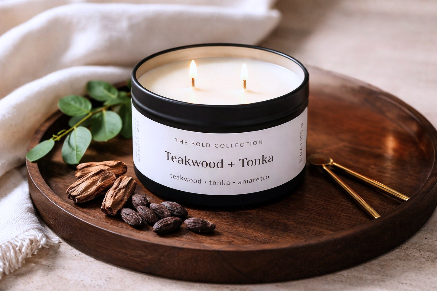 Candle labeled 'Teakwood + Tonka' on a wooden tray with cinnamon sticks and raisins.
