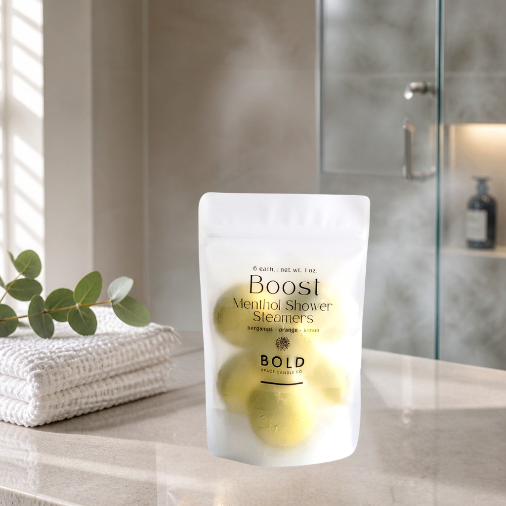 Shower steamers packaging on a bathroom counter with towels and a plant in the background