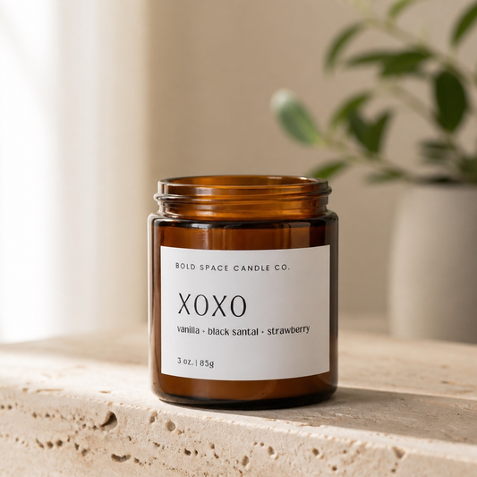 Brown candle jar with a label on a light surface, blurred plant in the background